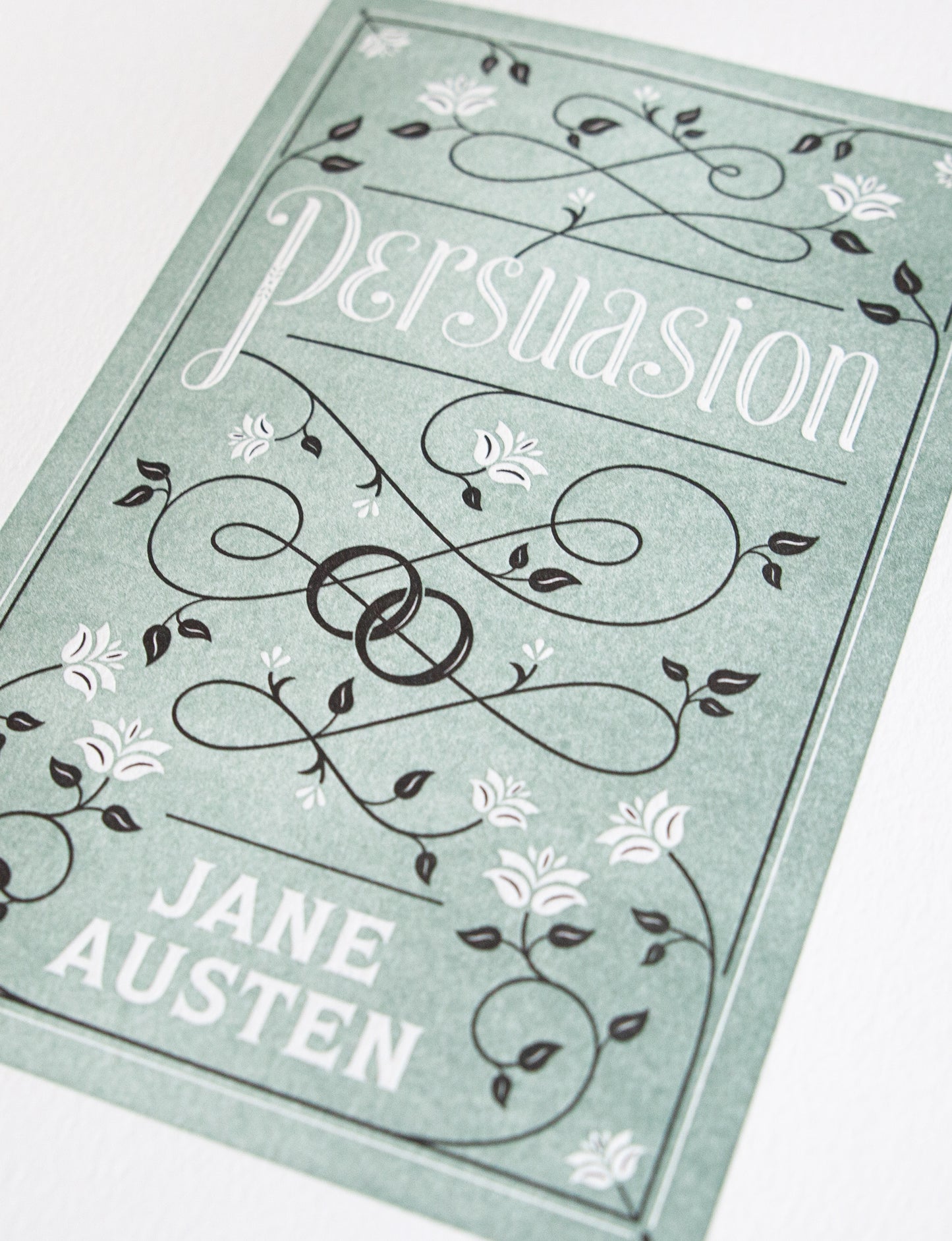 Close-up of a 2-color letterpress print in green and black. Printed artwork is an illustrated book cover of Persuasion including custom hand lettering.