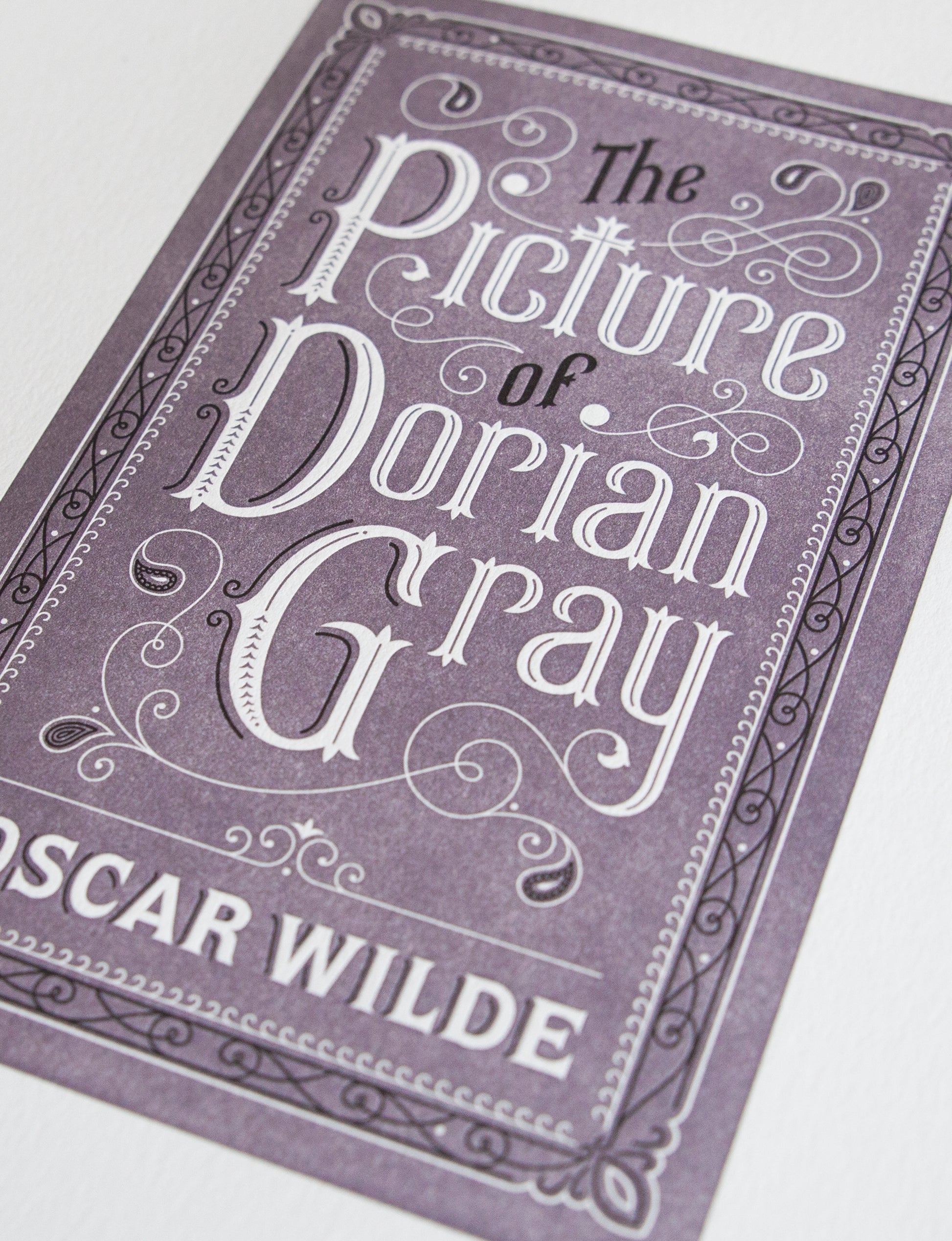 Close-up of a 2-color letterpress print in violet and black. Printed artwork is an illustrated book cover of The Picture of Dorian Gray including custom hand lettering.