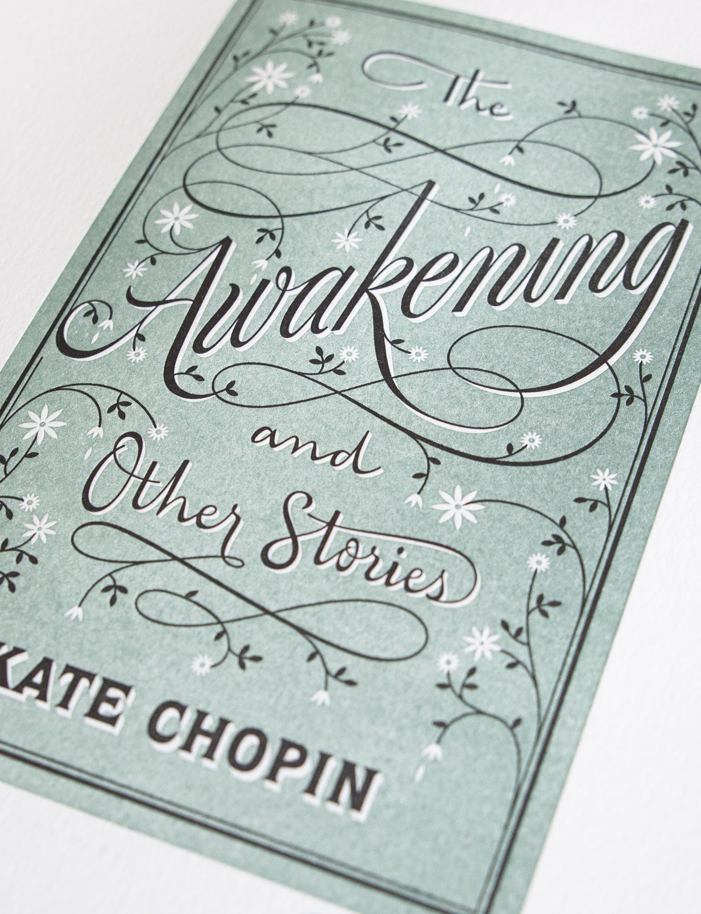 Close-up of a 2-color letterpress print in green and black. Printed artwork is an illustrated book cover of The Adventures of The Awakening including custom hand lettering.