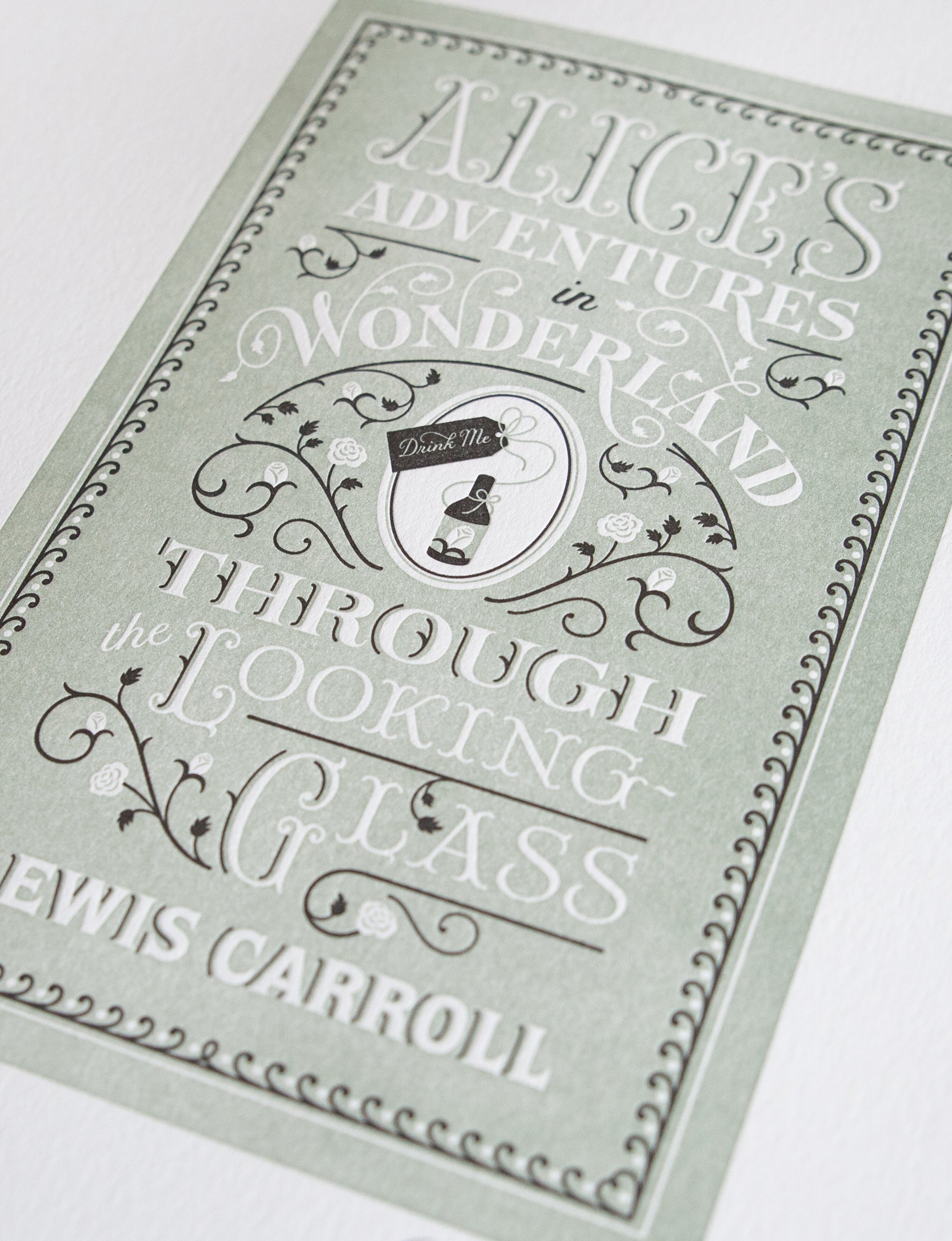 Close-up of a 2-color letterpress print in green and black. Printed artwork is an illustrated book cover of Alice's Adventures in Wonderland including custom hand-lettering.