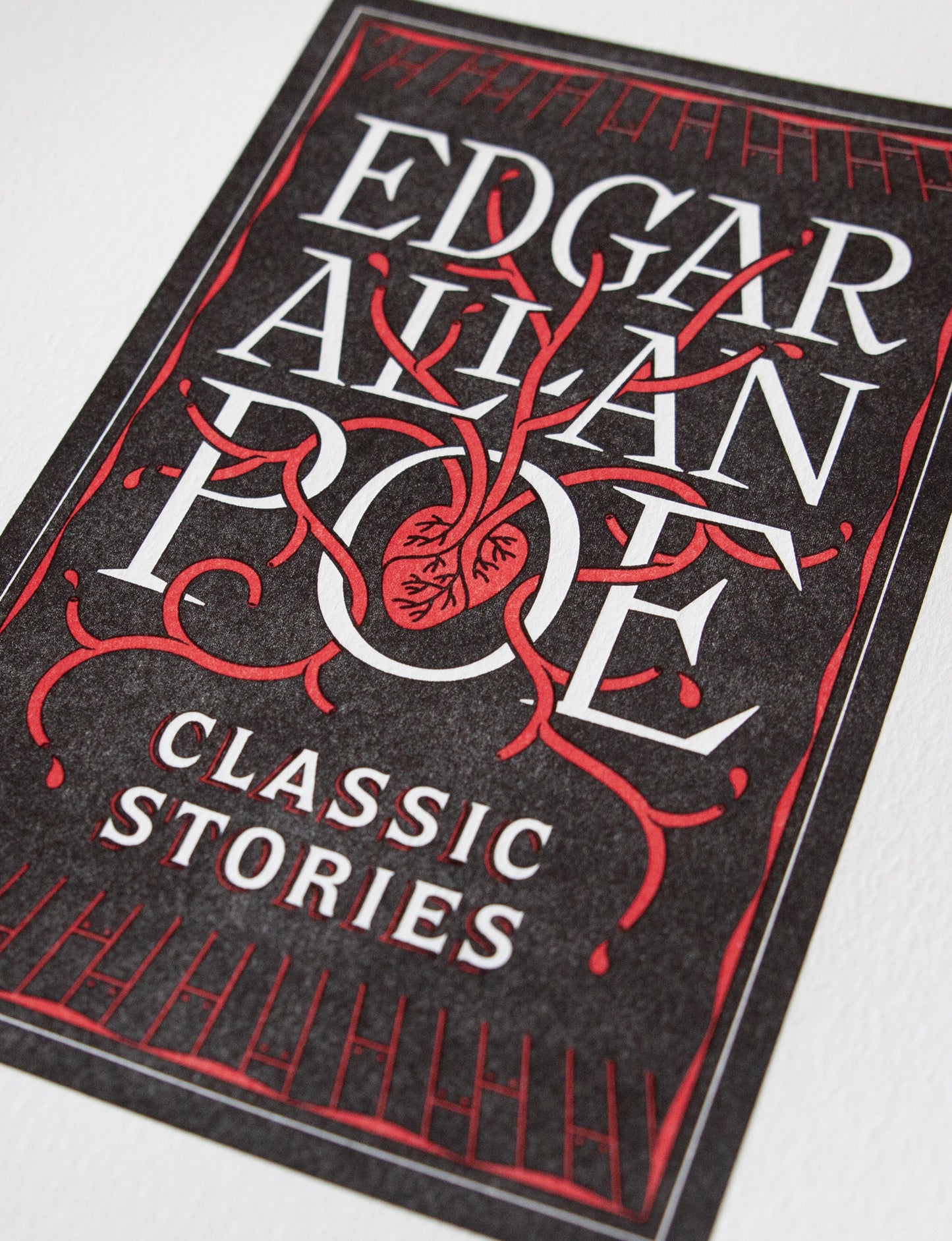 Close-up of a 2-color letterpress print in black and red. Printed artwork is an illustrated book cover of Edgar Allan Poe including custom hand lettering.