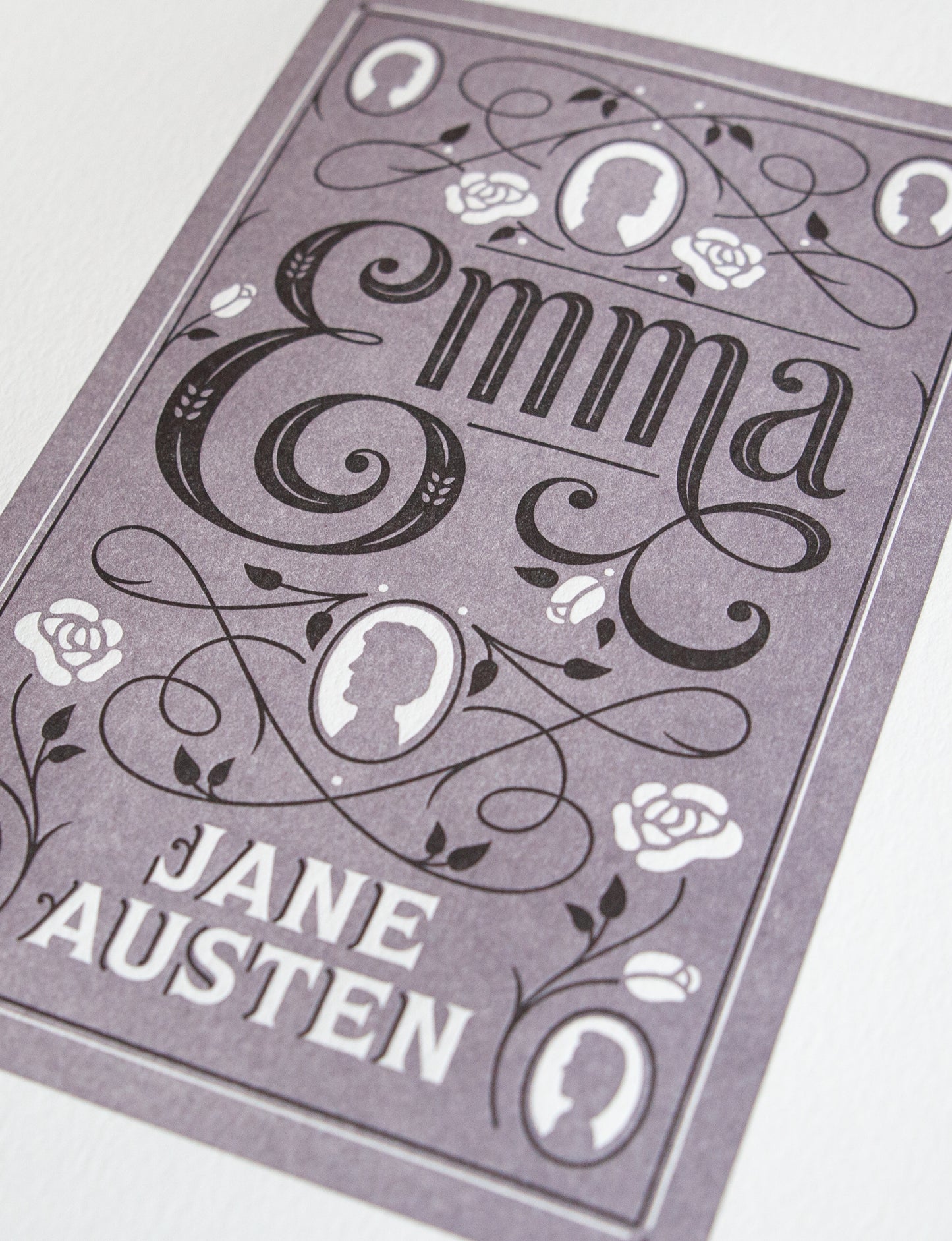 Close-up of a 2-color letterpress print in violet and black. Printed artwork is an illustrated book cover of Emma including custom hand lettering.