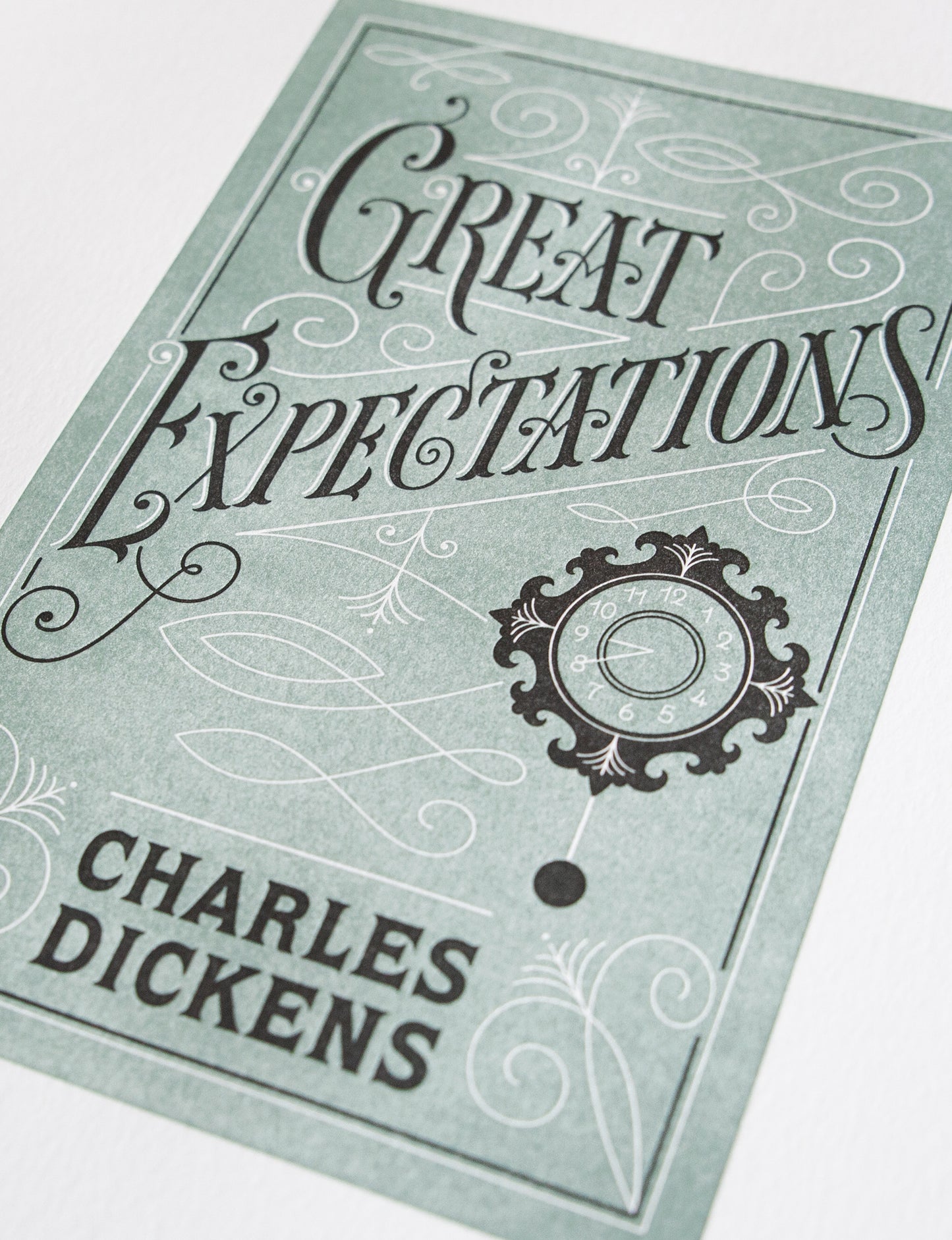 Close-up of a 2-color letterpress print in green and black. Printed artwork is an illustrated book cover of Great Expectations including custom hand lettering.
