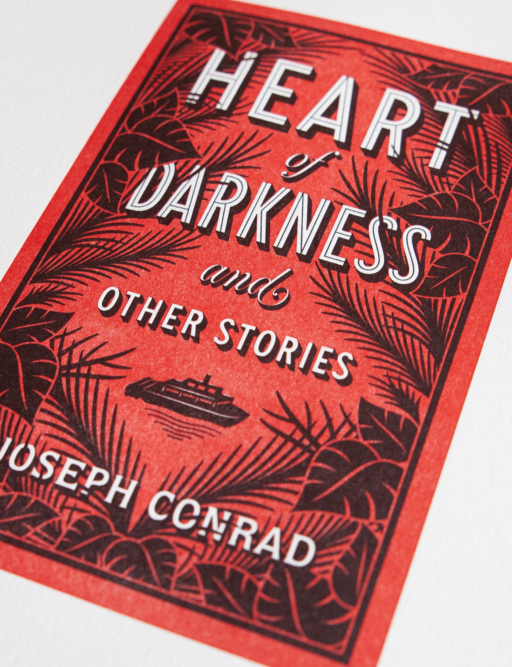 Close-up of a 2-color letterpress print in red and black. Printed artwork is an illustrated book cover of Heart of Darkness including custom hand lettering.