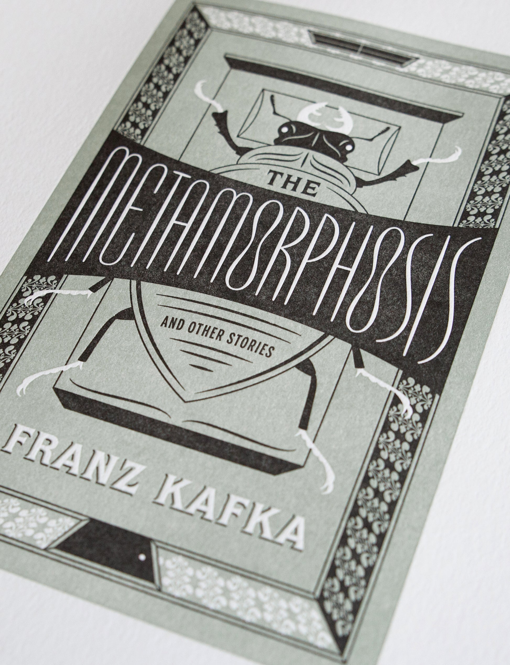 Close-up of a 2-color letterpress print in green and black. Printed artwork is an illustrated book cover of The Metamorphosis including custom hand lettering.