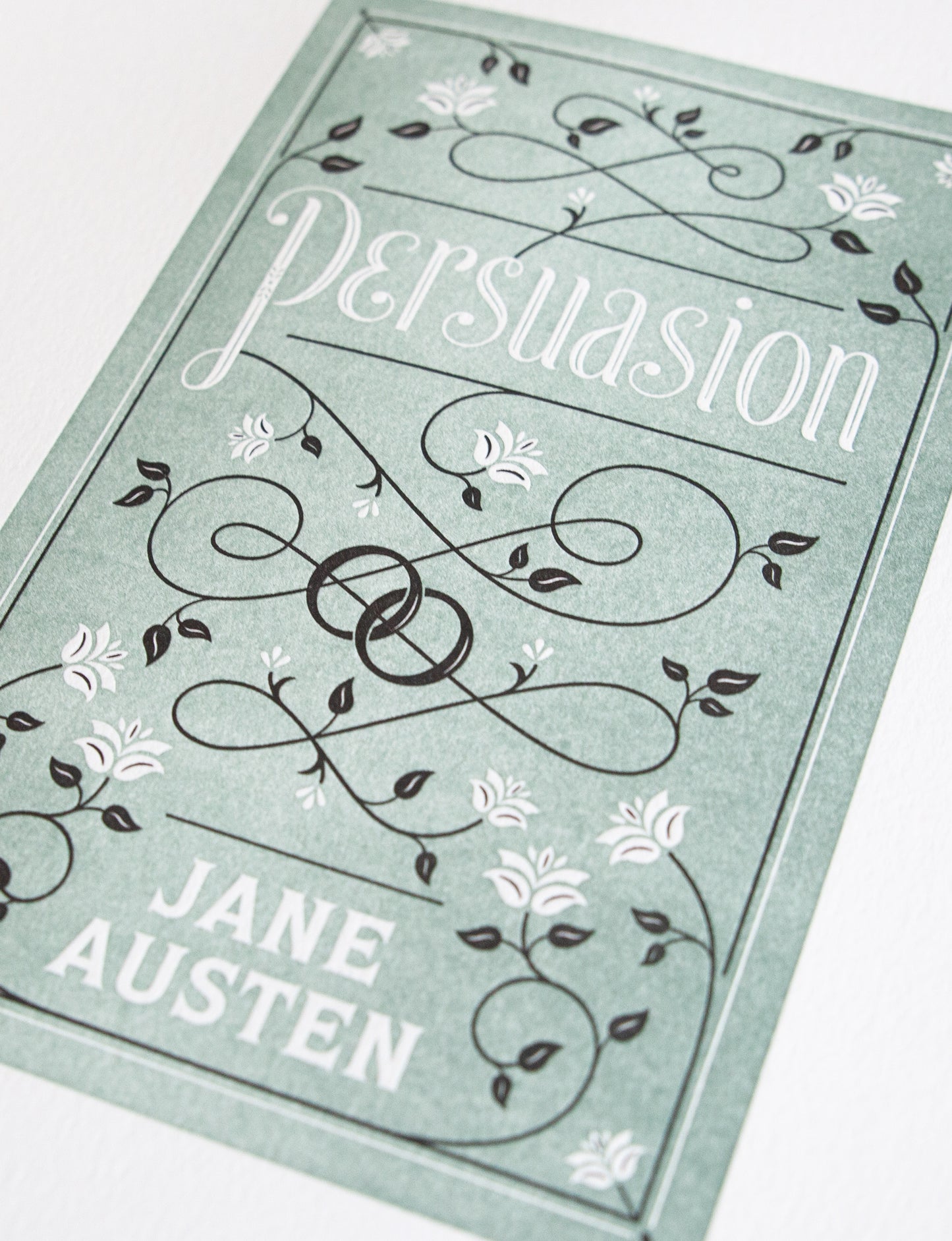 Close-up of a 2-color letterpress print in green and black. Printed artwork is an illustrated book cover of Persuasion including custom hand lettering.