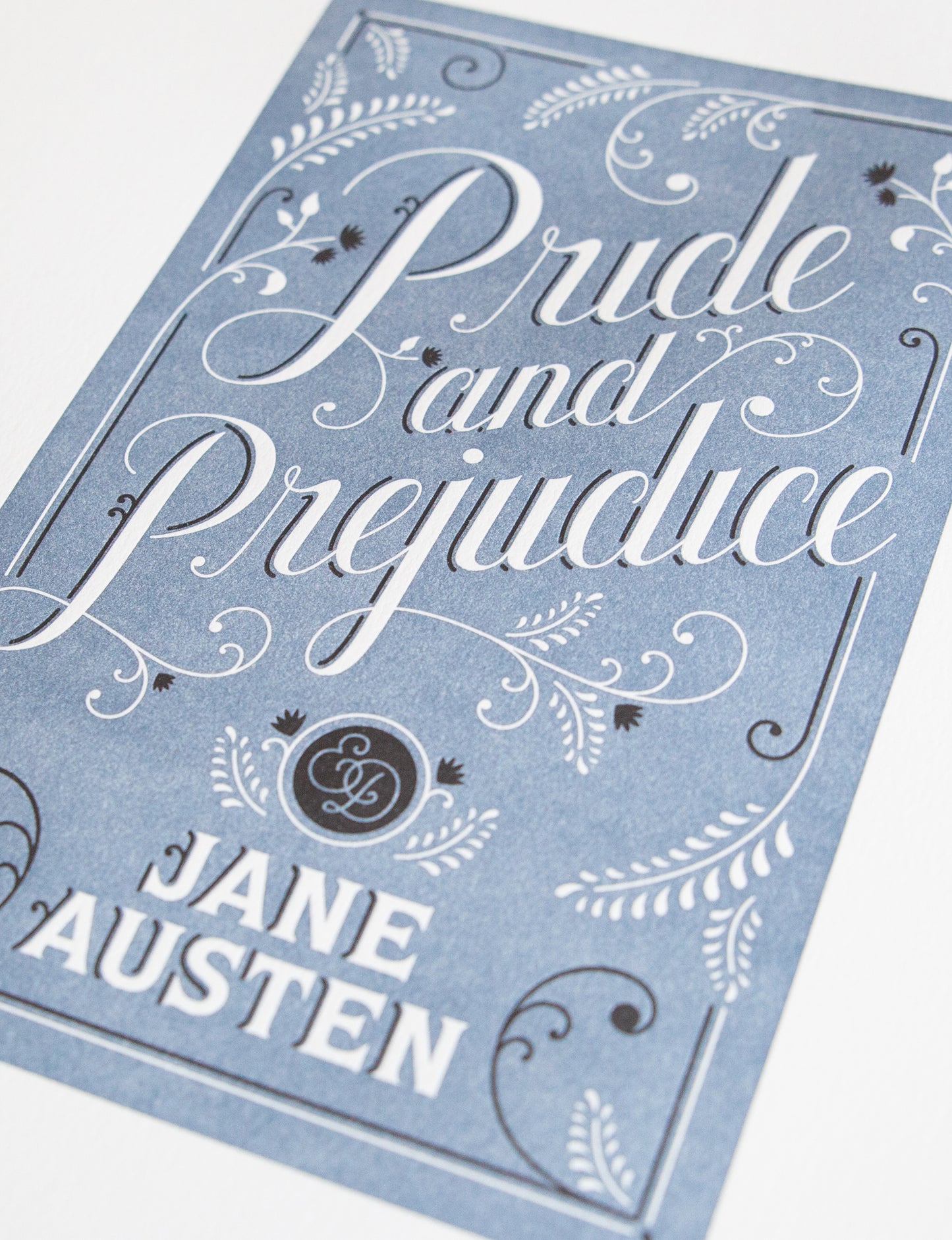 Close-up of a 2-color letterpress print in blue and black. Printed artwork is an illustrated book cover of Pride and Prejudice including custom hand lettering.