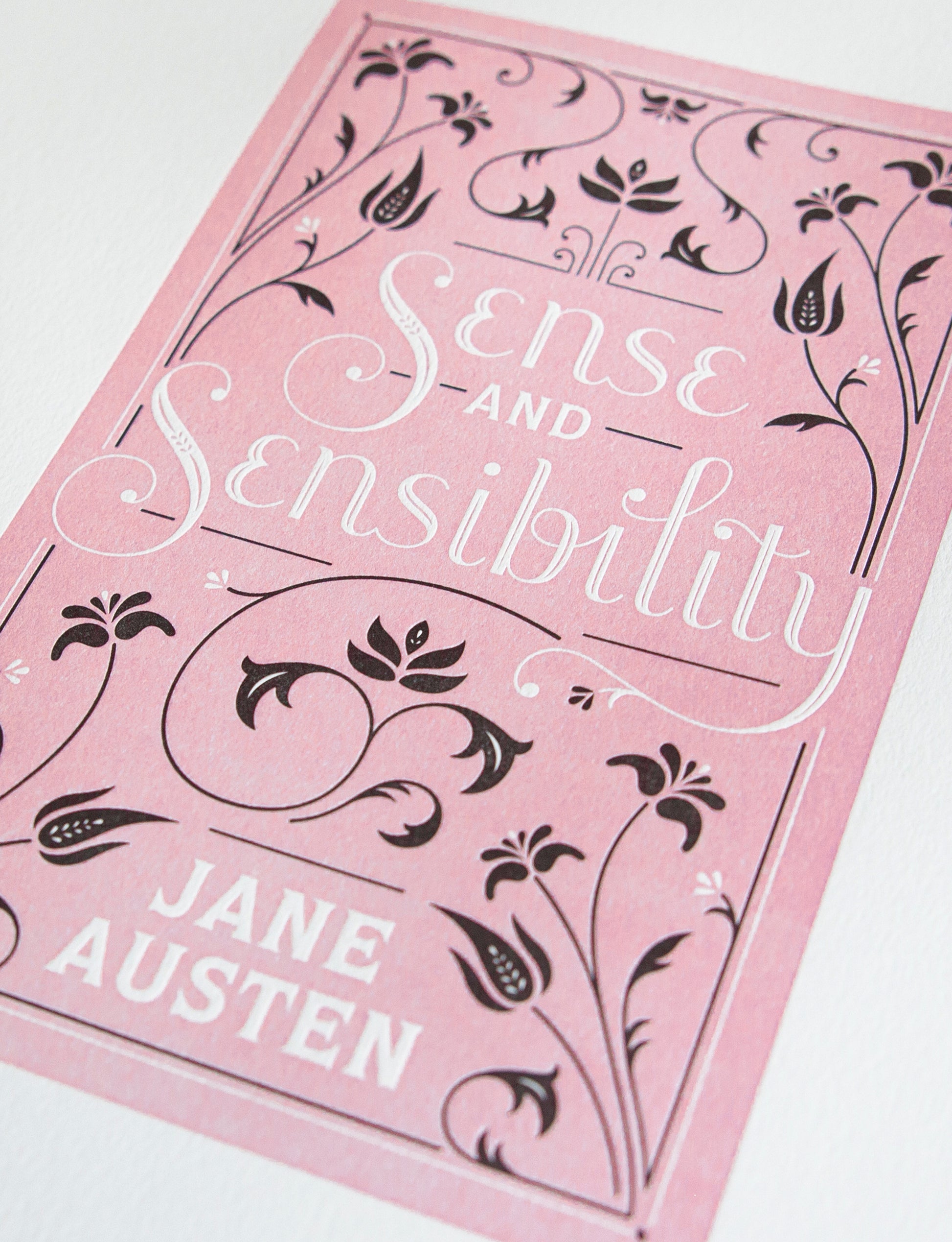 Close-up of a 2-color letterpress print in pink and black. Printed artwork is an illustrated book cover of Sense and Sensibility including custom hand lettering.