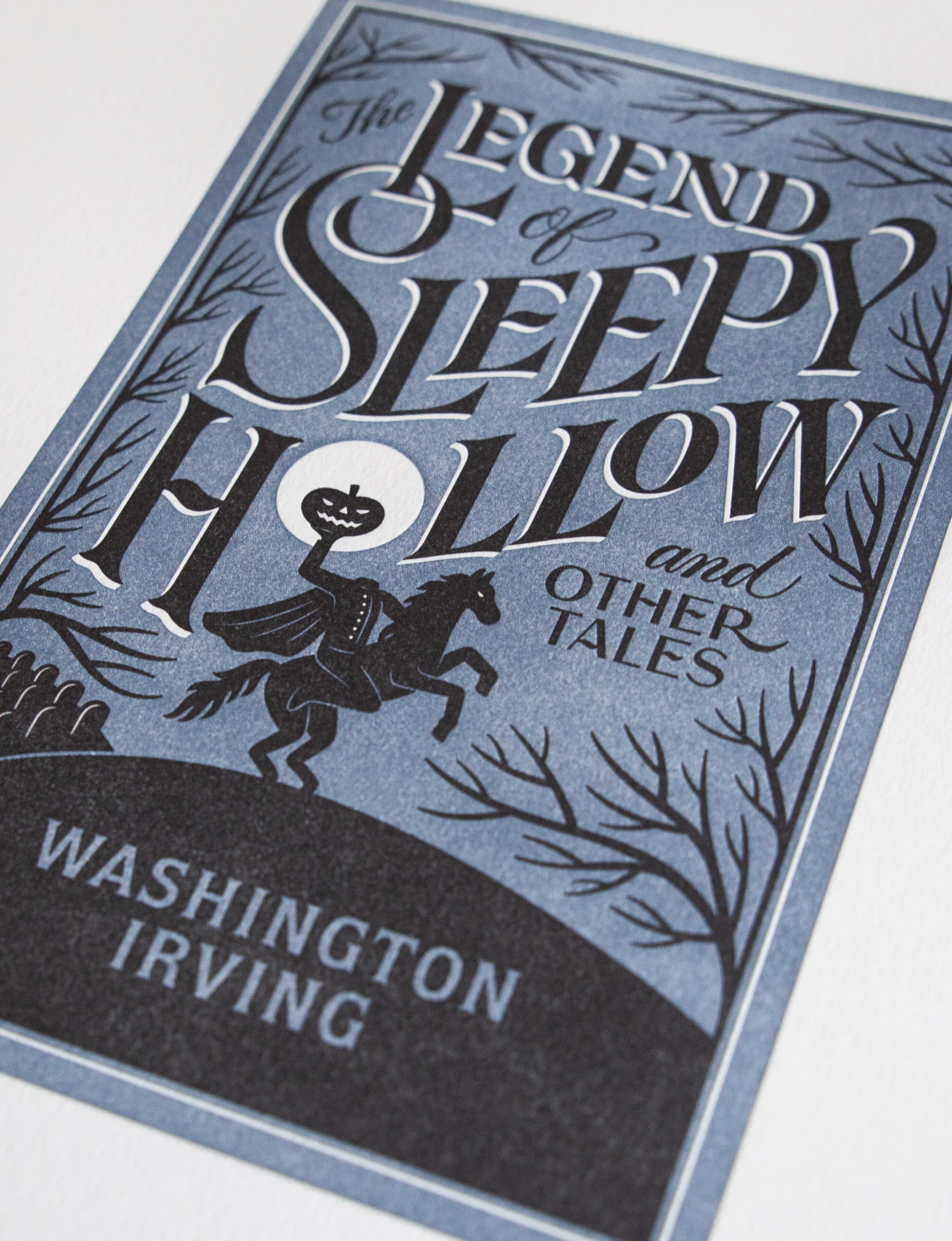 Close-up of a 2-color letterpress print in blue and black. Printed artwork is an illustrated book cover of The Legend of Sleepy Hollow including custom hand lettering.