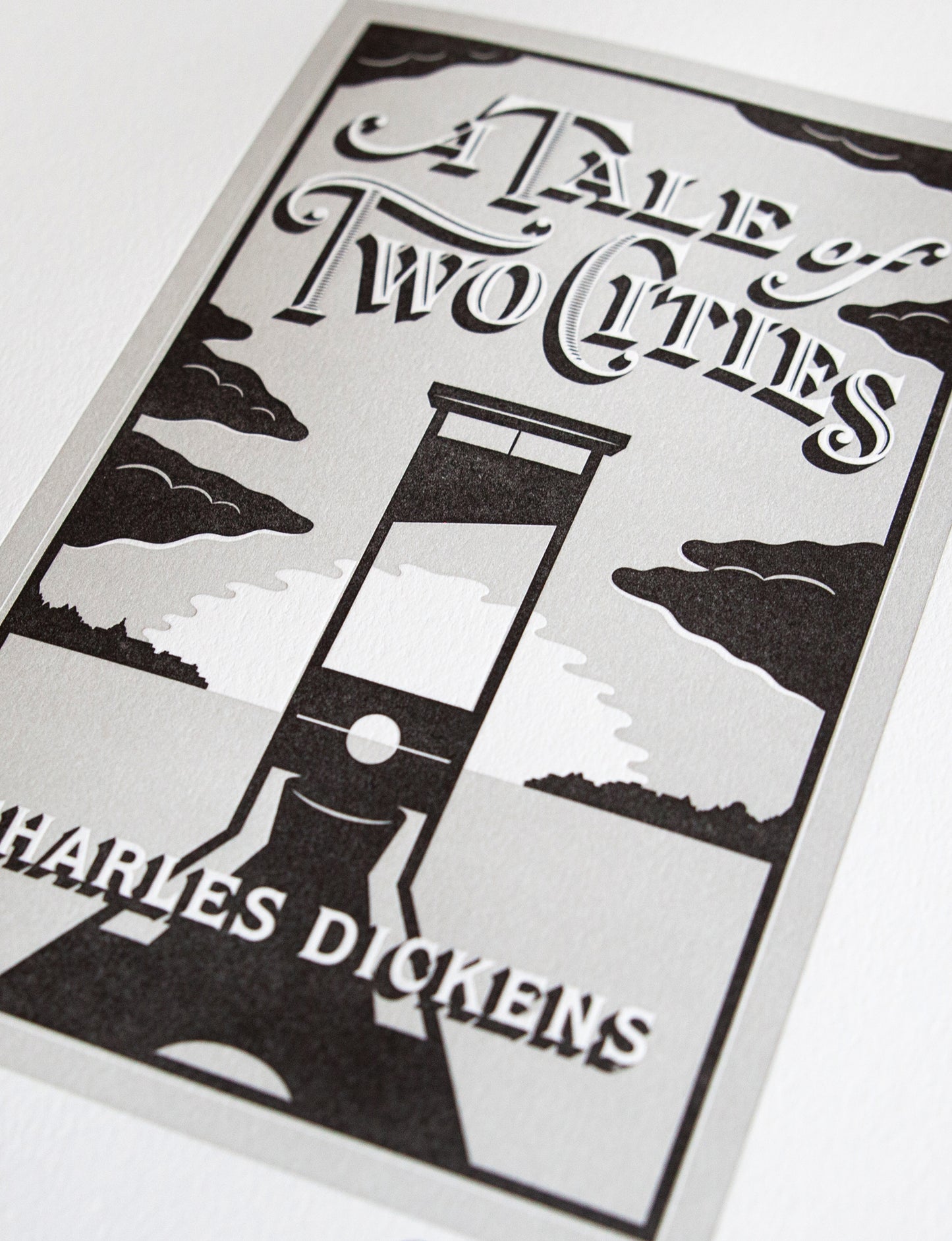Close-up of a 2-color letterpress print in gray and black. Printed artwork is an illustrated book cover of A Tale of Two Cities including custom hand lettering.