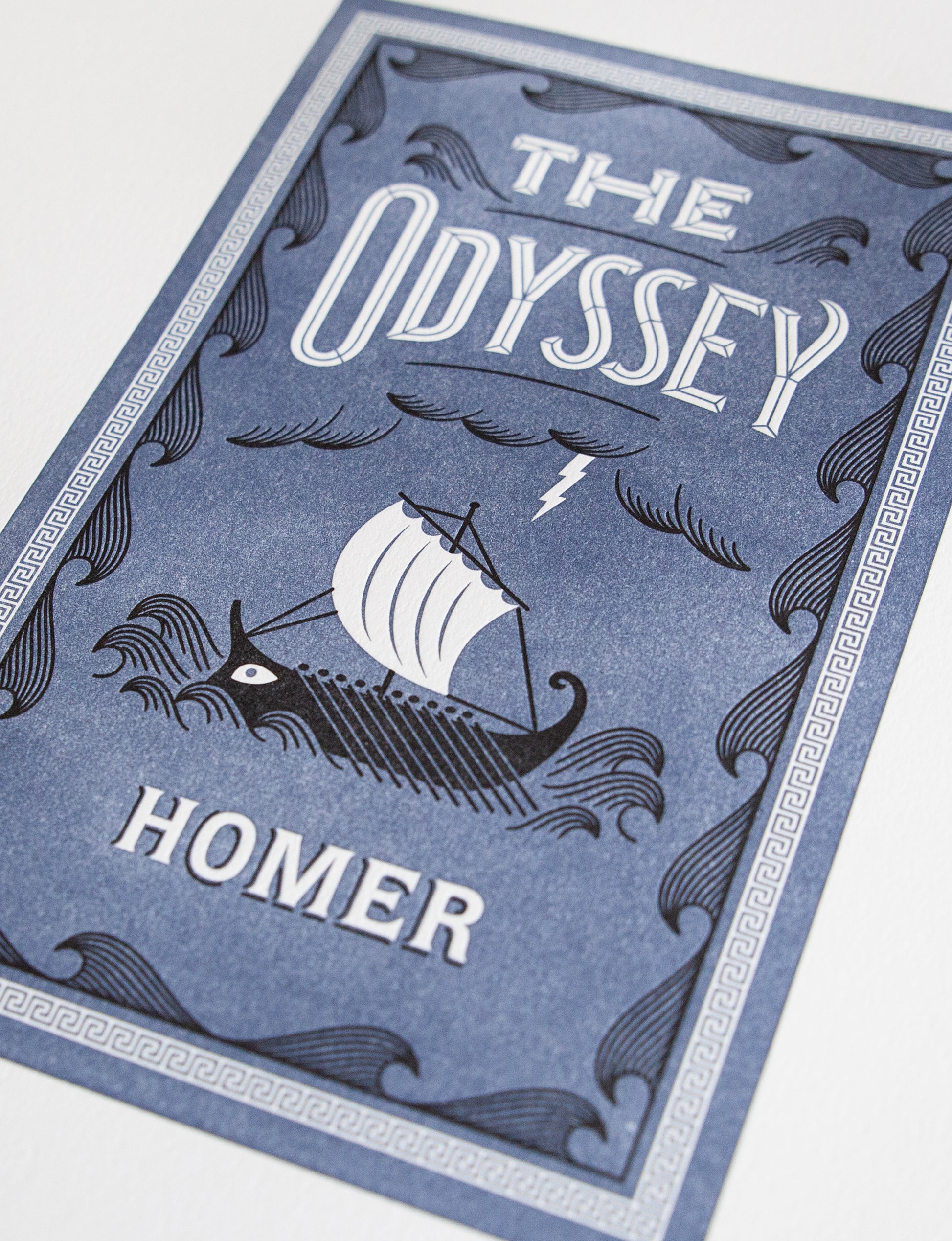 Close-up of a 2-color letterpress print in blue and black. Printed artwork is an illustrated book cover of The Adventures of The Odyssey including custom hand lettering.