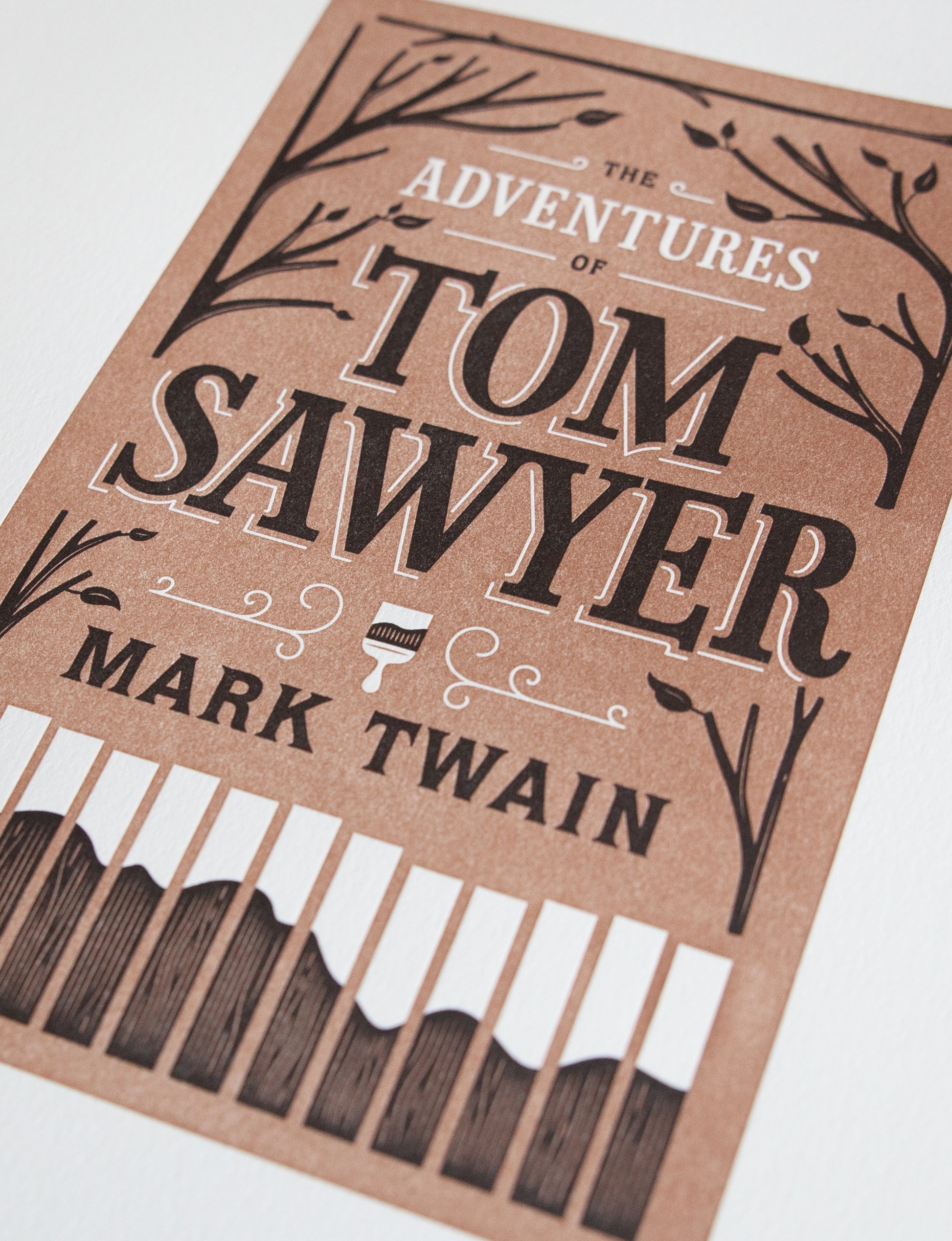Close-up of a 2-color letterpress print in brown and black. Printed artwork is an illustrated book cover of The Adventures of Tom Sawyer including custom hand lettering.